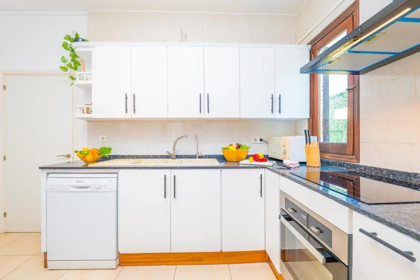 A bright kitchen with white cabinets, a sink, and a cooking area.