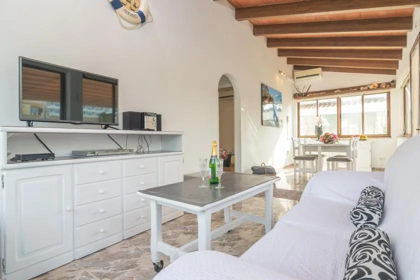 A living room with a coffee table and white seating, opening onto a dining area.