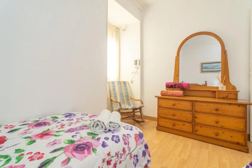 A bedroom with floral bedding, a wooden dresser, and a rocking chair.