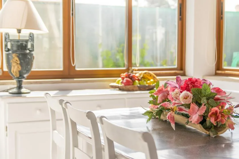 A bright dining area with a table set beside large windows and fresh flowers.