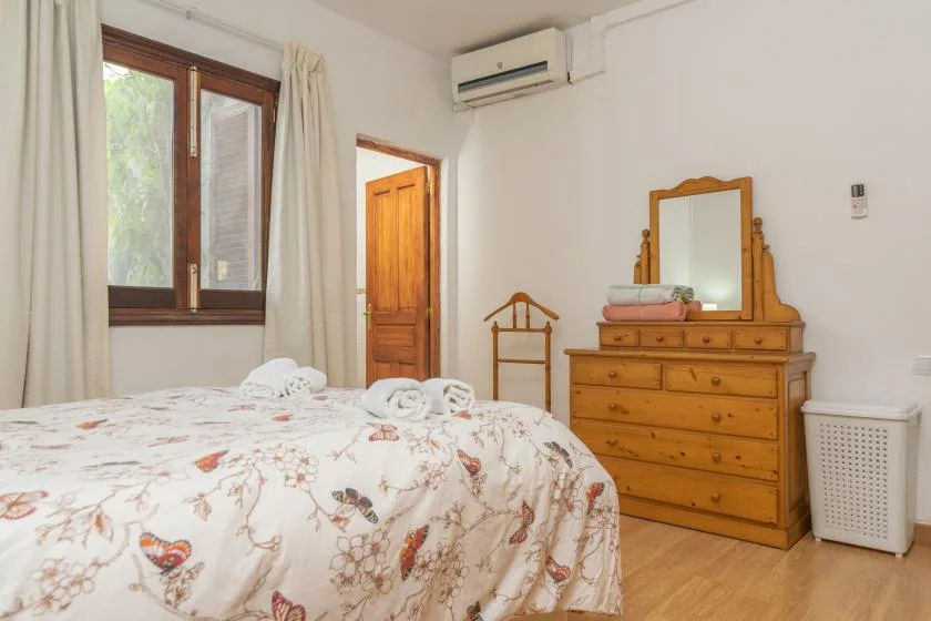 A bedroom with a floral-covered bed and a wooden dresser beside the window.