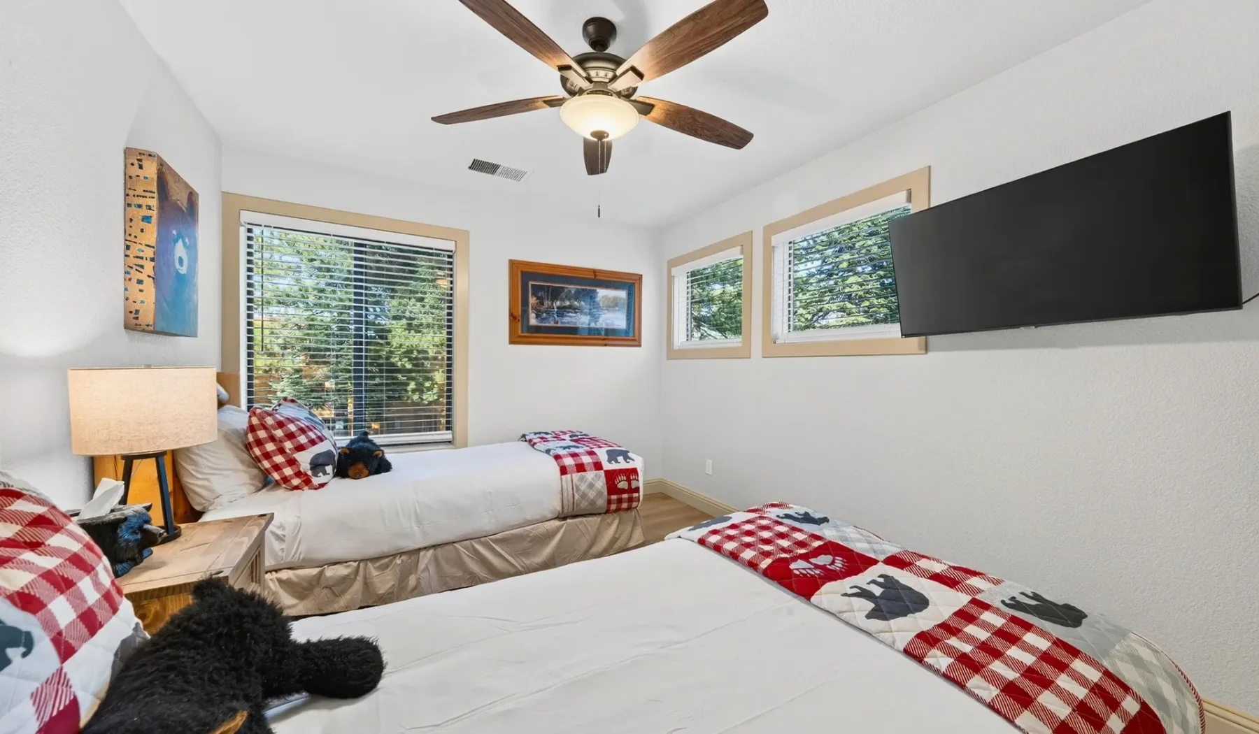 Un dormitorio con dos camas, ventanas y un televisor montado en la pared.