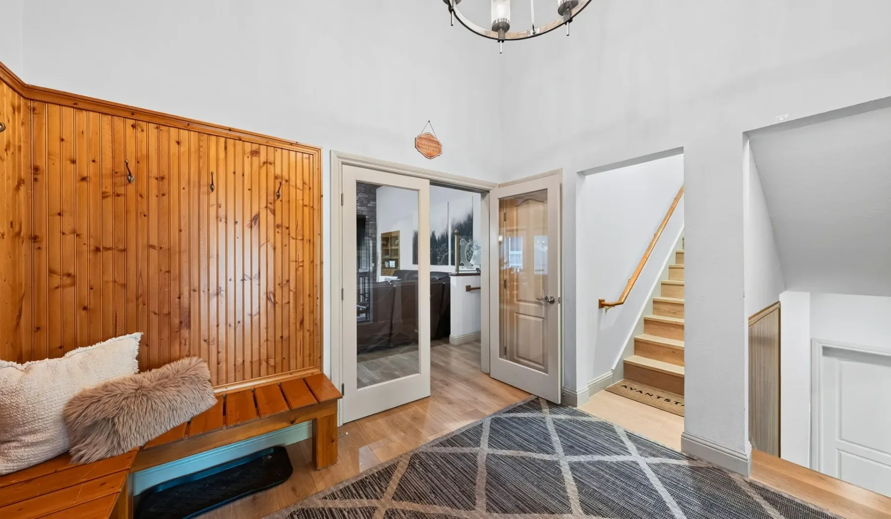 Una entrada luminosa con un banco de madera, puertas de vidrio y escaleras.