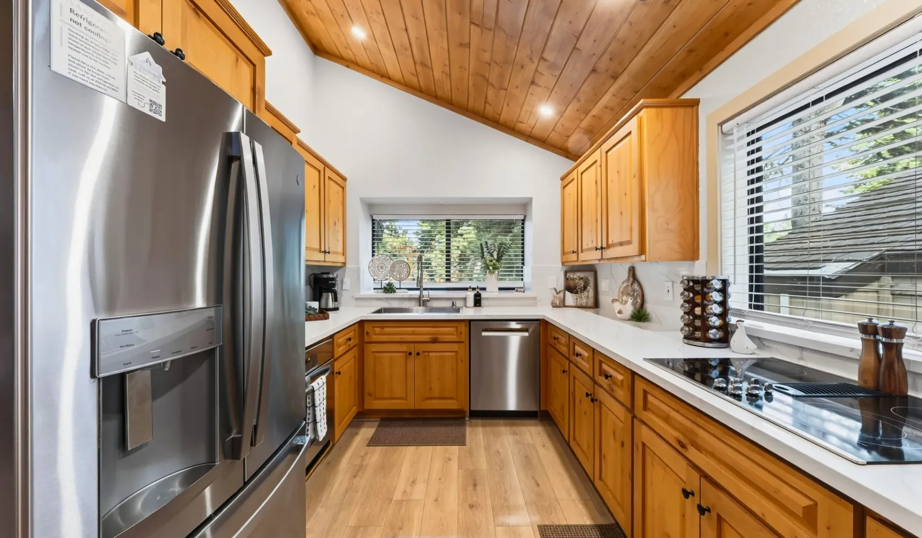Una cocina con gabinetes de madera, electrodomésticos de acero inoxidable y ventanas con persianas.