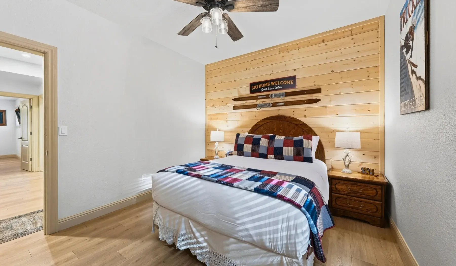 Un dormitorio con una cama vestida con ropa de cama colorida y estampada frente a una pared revestida de madera.