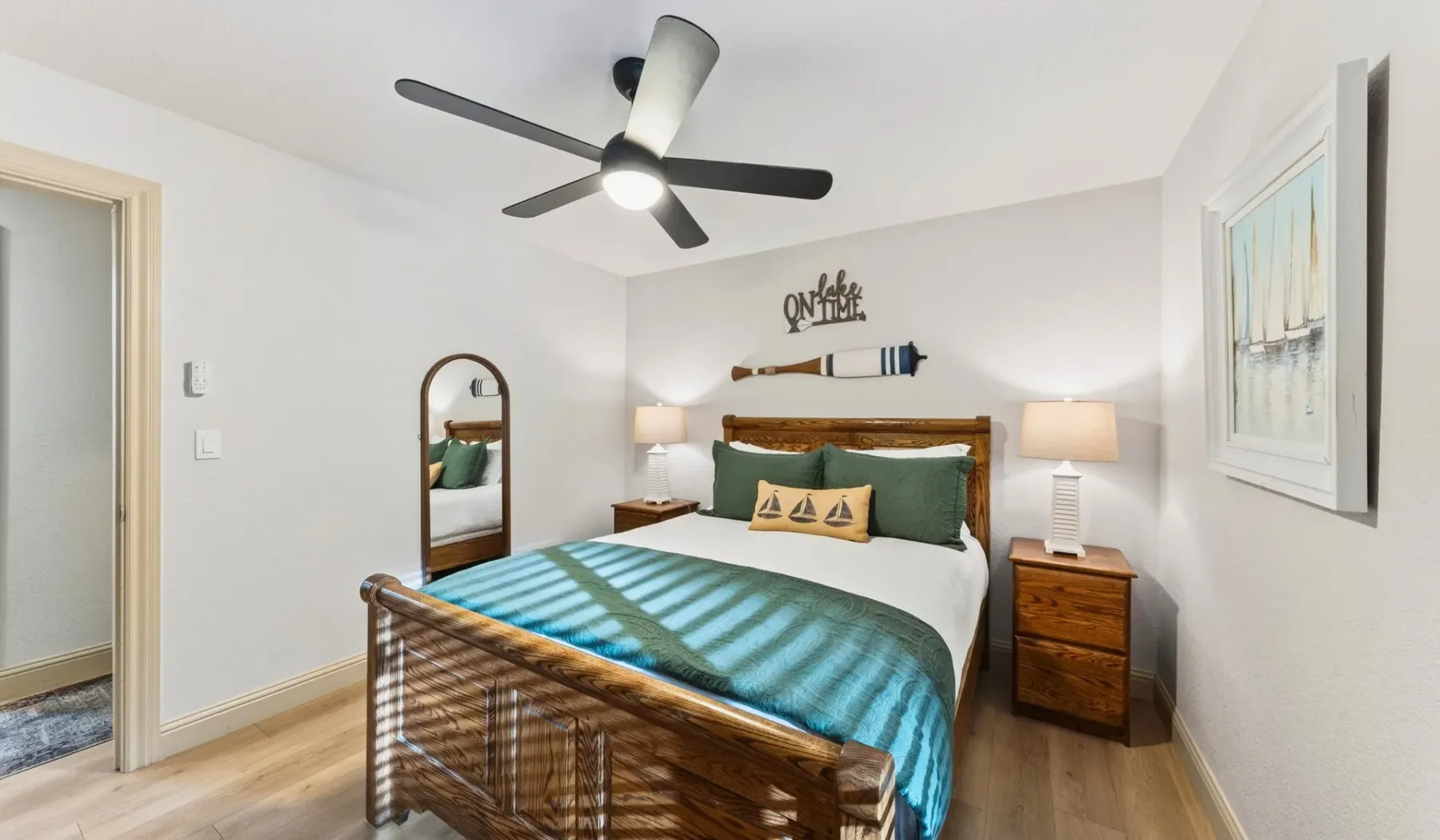 Un dormitorio con una cama de madera, ropa de cama verde azulado y mesitas a juego.