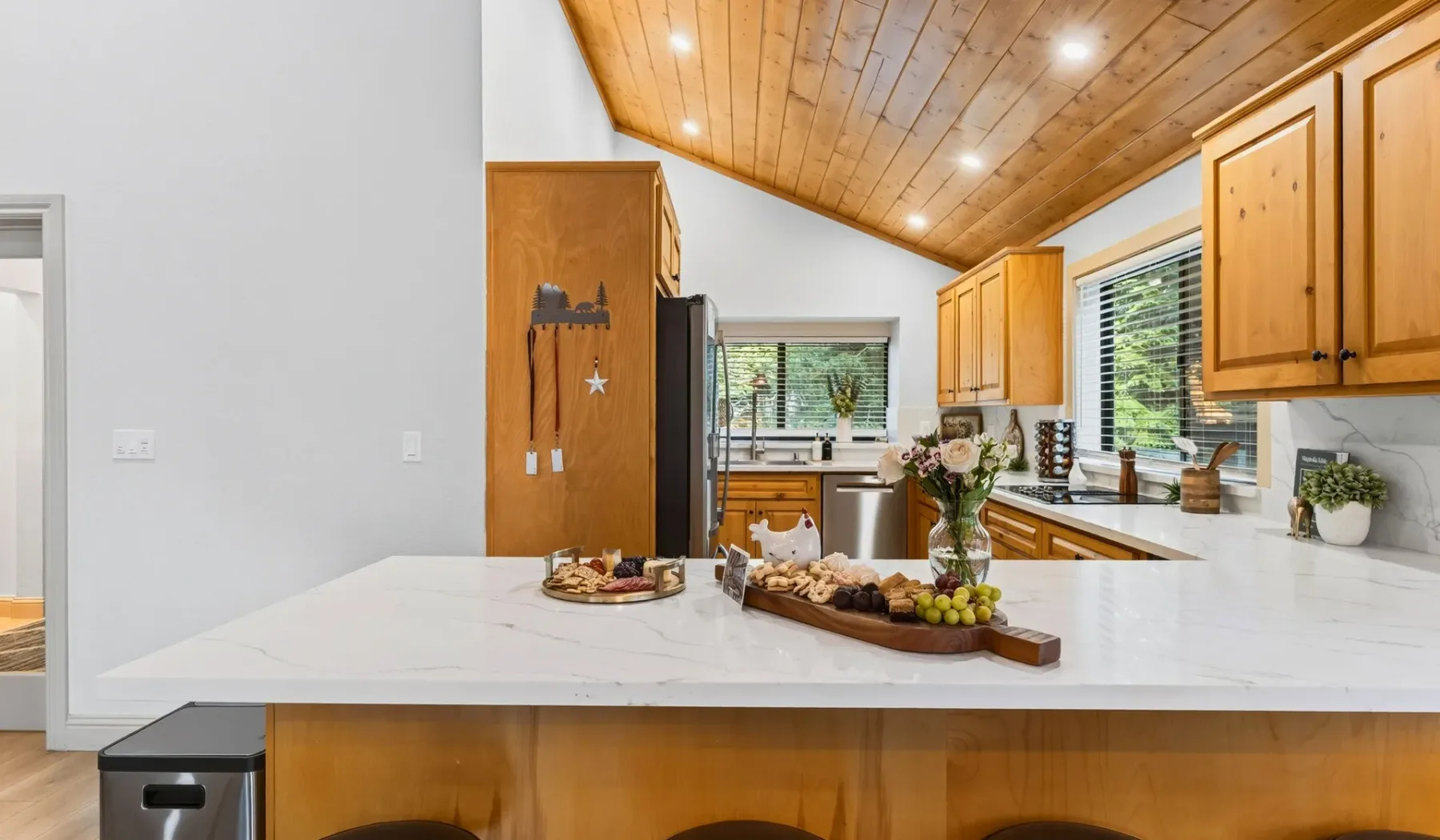 Una cocina luminosa con isla blanca, gabinetes de madera y techo revestido de madera.