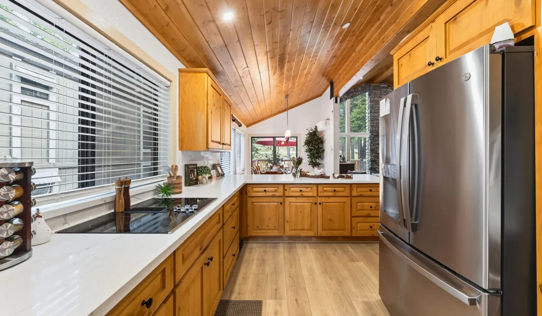 Una cocina luminosa con gabinetes de madera, encimeras blancas y un refrigerador de acero inoxidable.