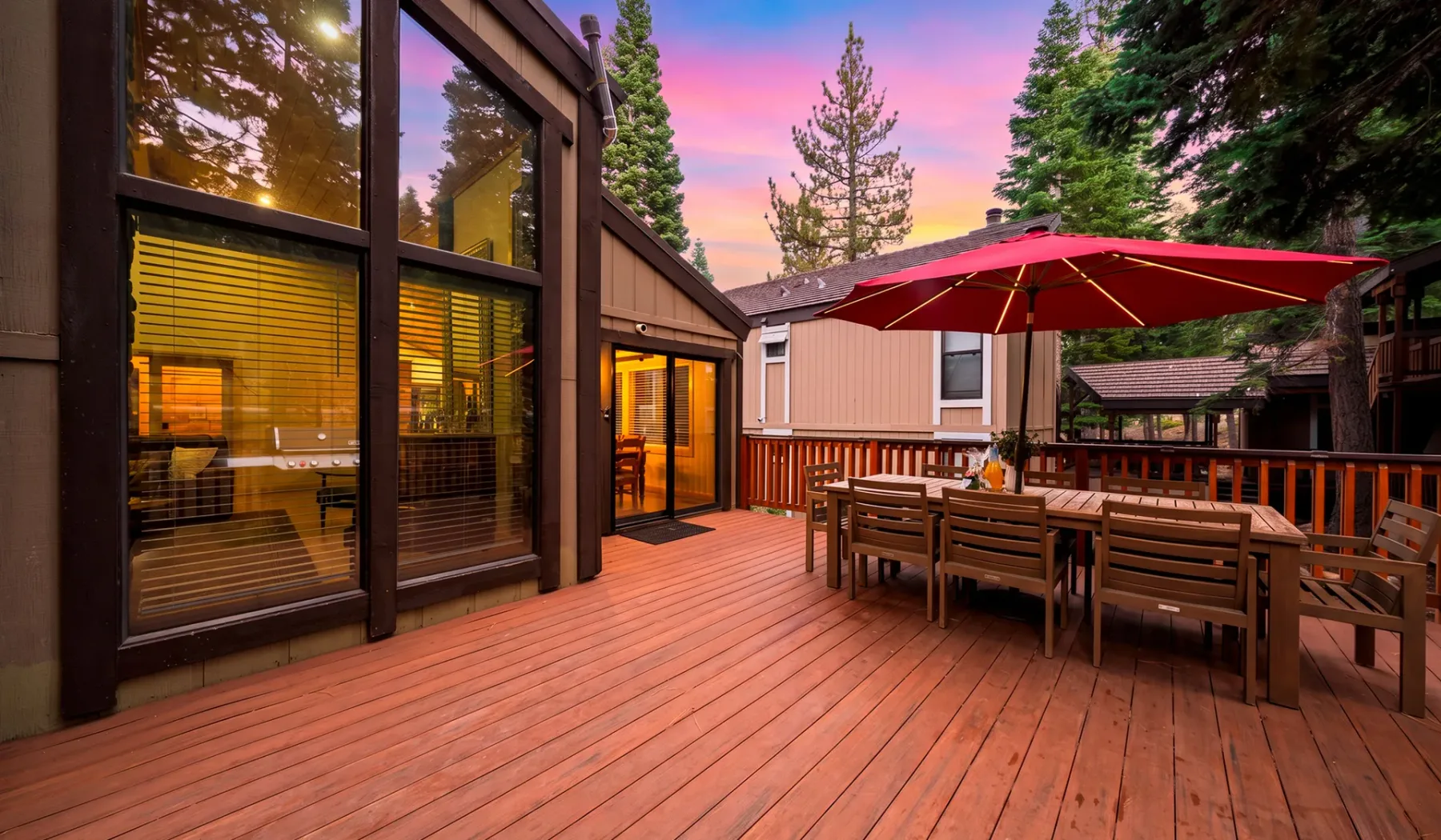 Una terraza de madera junto a una casa moderna tiene un comedor al aire libre bajo una sombrilla roja.
