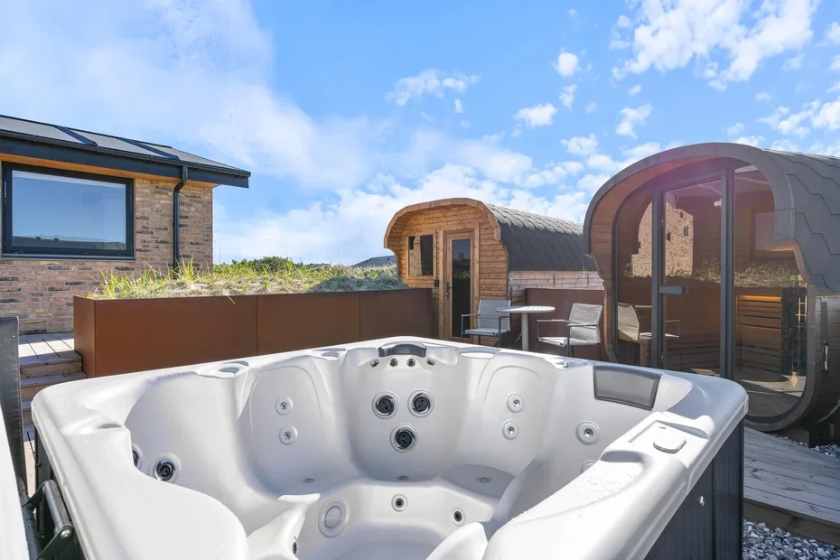 Una bañera de hidromasaje al aire libre está en una terraza junto a cabañas de madera redondeadas.