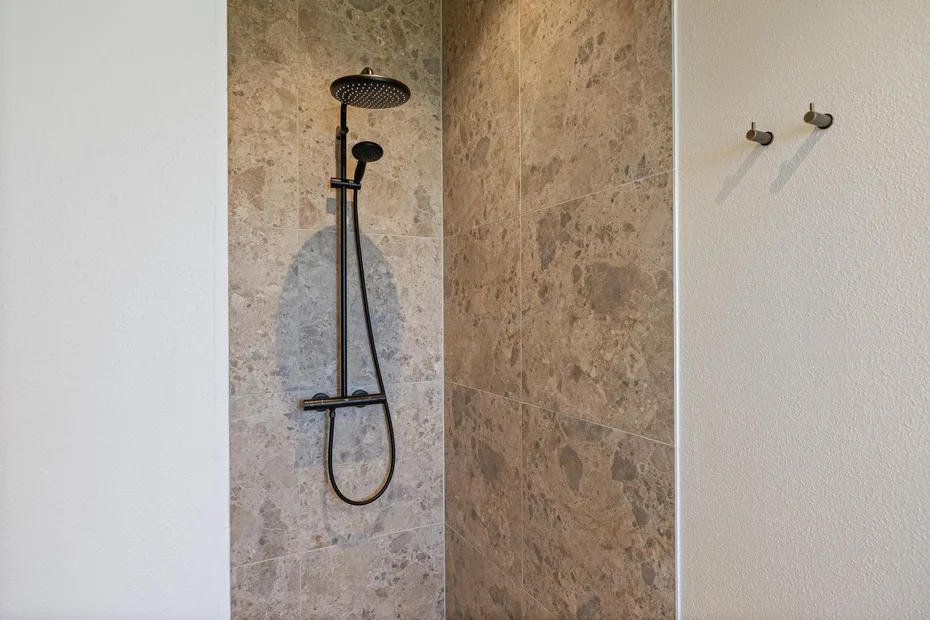Una ducha de baño con accesorios oscuros frente a paredes con diseño de piedra.