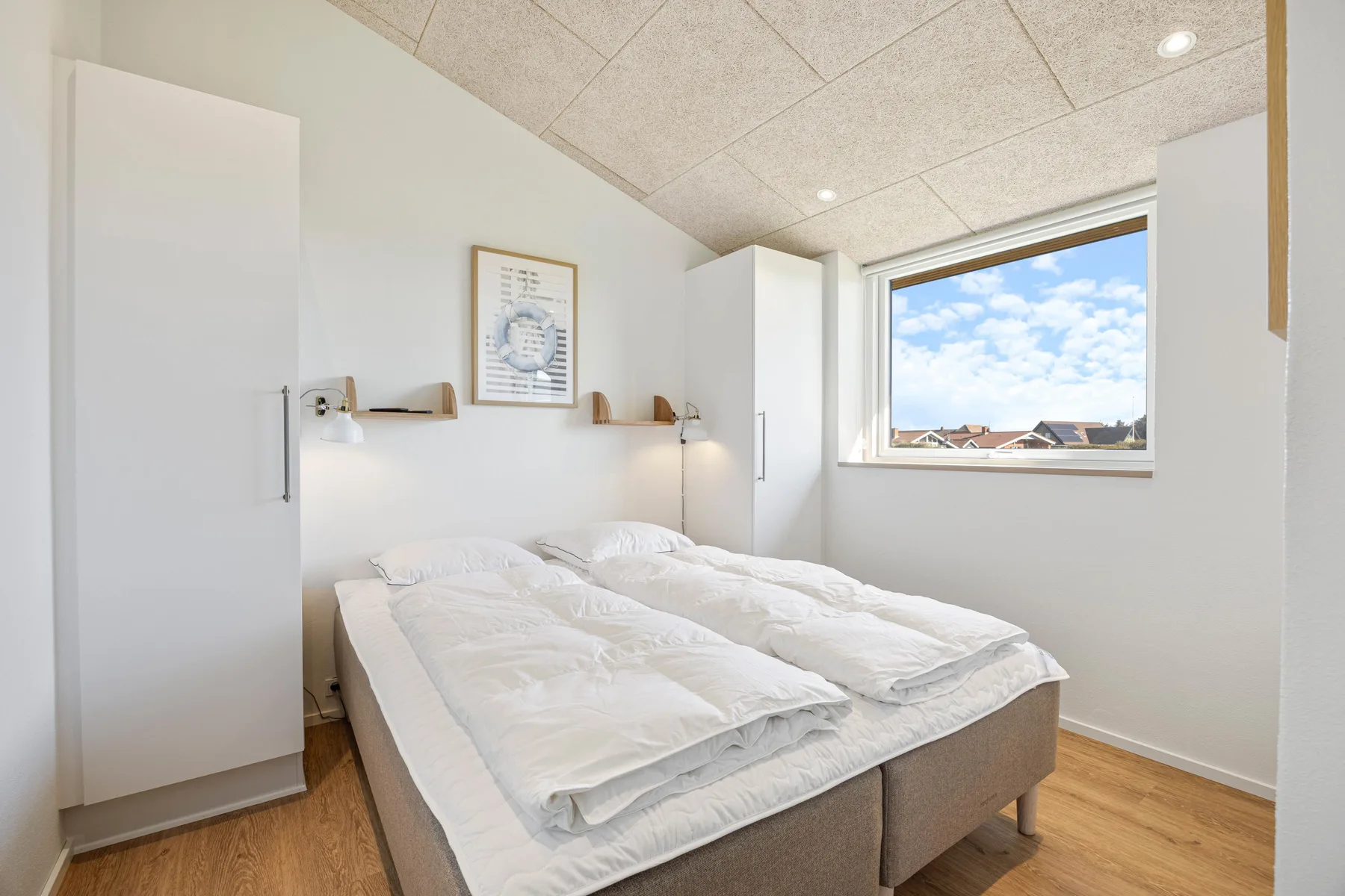 Dormitorio luminoso con una cama doble y una ventana con vistas a los tejados.