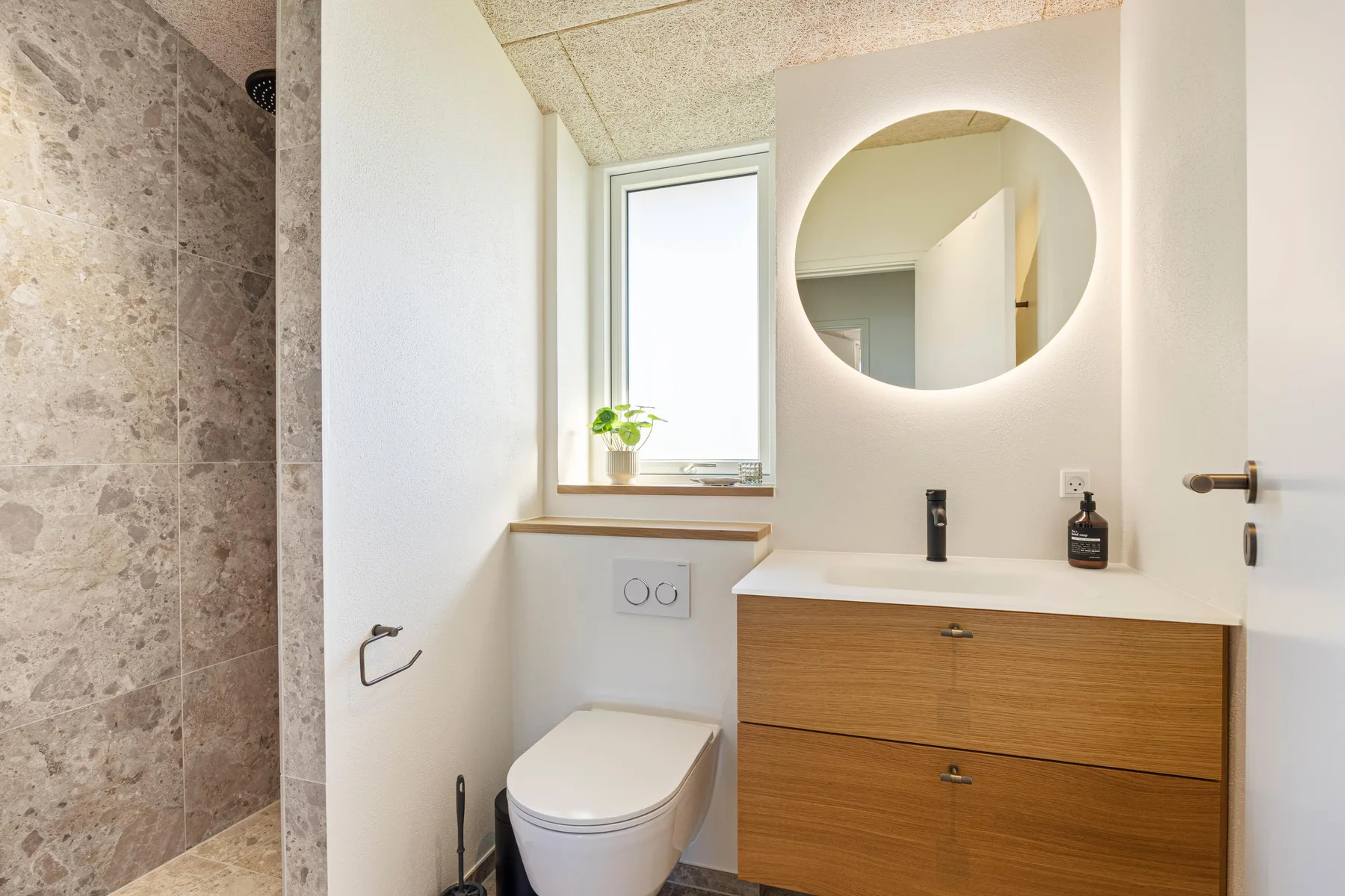 Un baño luminoso con ducha, inodoro y mueble de lavabo con frentes de madera.