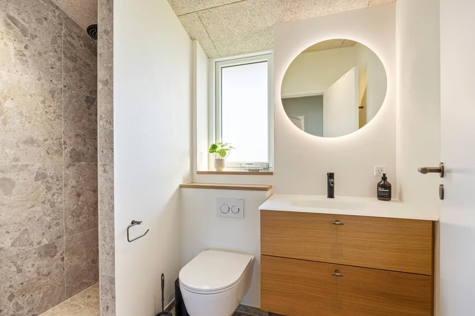 Un baño luminoso con ducha de vidrio, inodoro y lavabo con mueble de madera.
