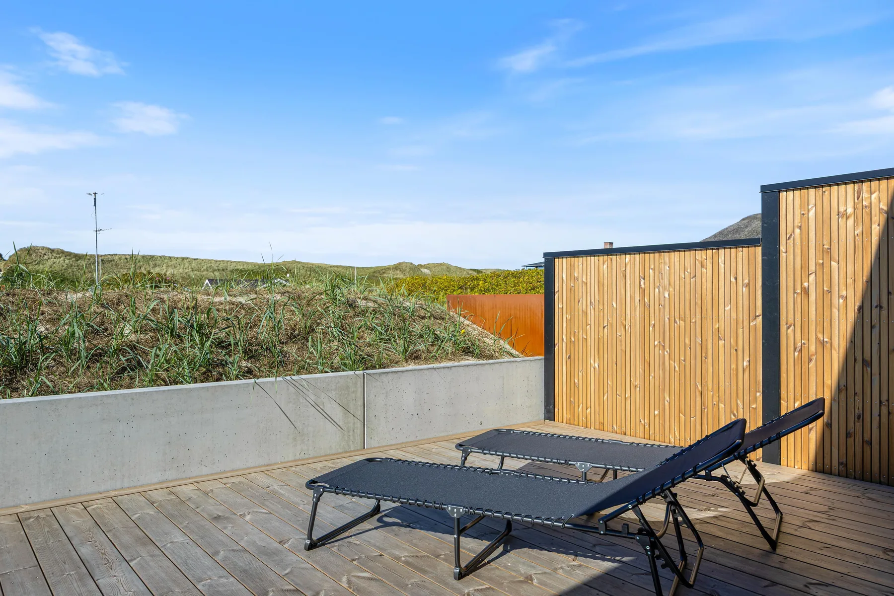 Una terraza exterior con tumbonas reclinables junto a una pantalla de madera.