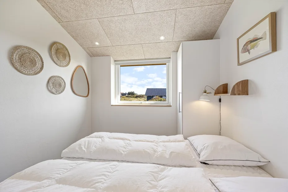 Un dormitorio luminoso con ropa de cama blanca y una ventana con vistas al paisaje.