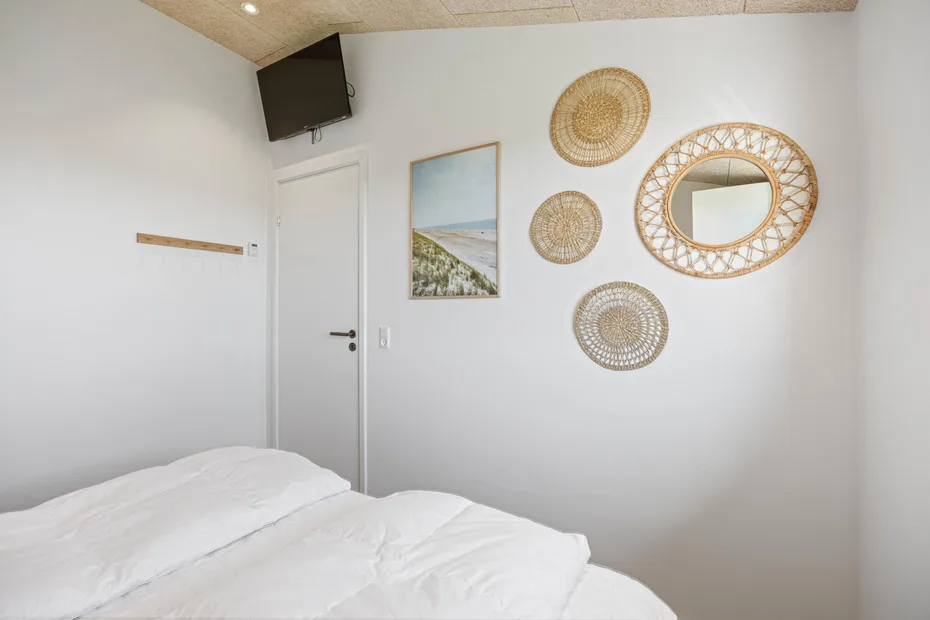 Un dormitorio con ropa de cama blanca y adornos tejidos en la pared.