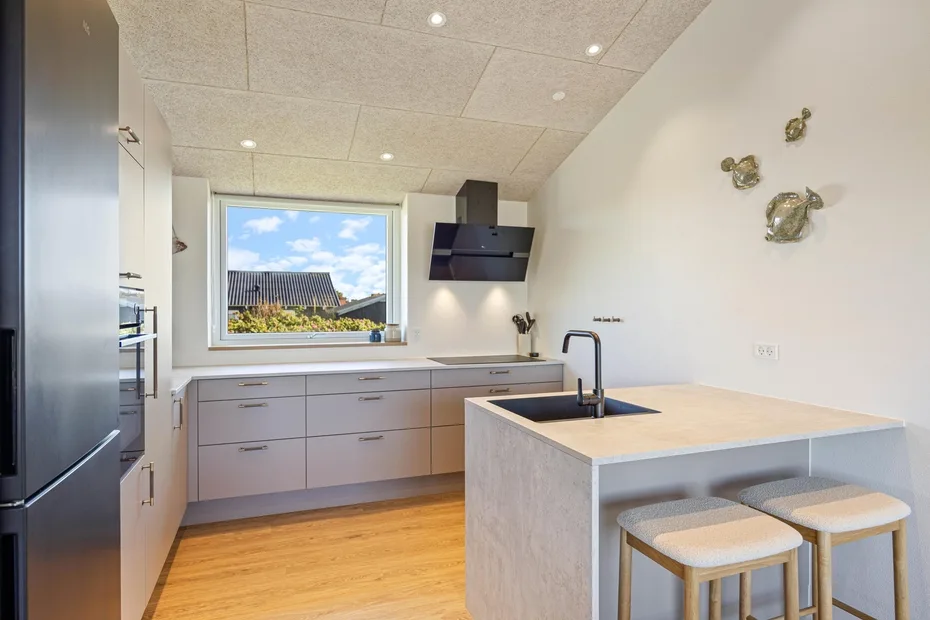 Una cocina luminosa con gabinetes claros, una isla central y una ventana con vista a tejados.