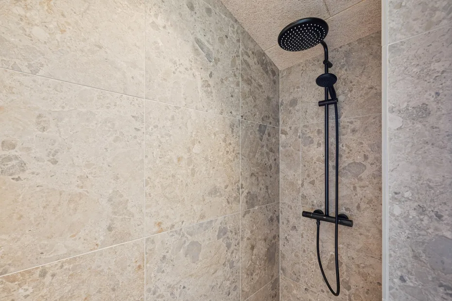Una ducha revestida de azulejos con un cabezal oscuro y una ducha de mano.