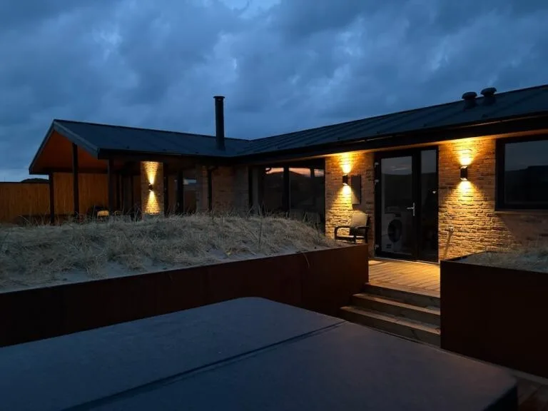 Exterior de una casa moderna al anochecer, con luces cálidas que iluminan la entrada.