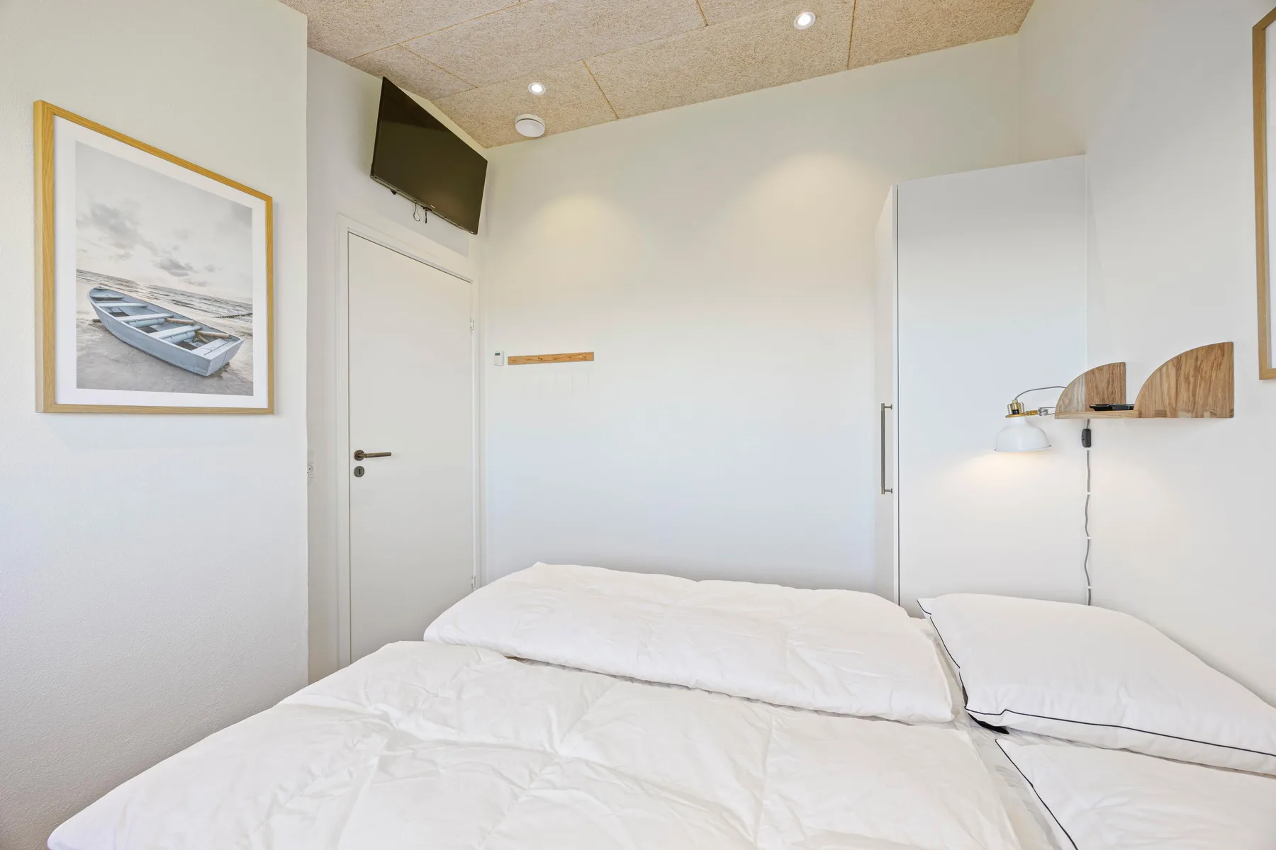 Un dormitorio con una cama, una imagen enmarcada y un televisor montado en la pared.
