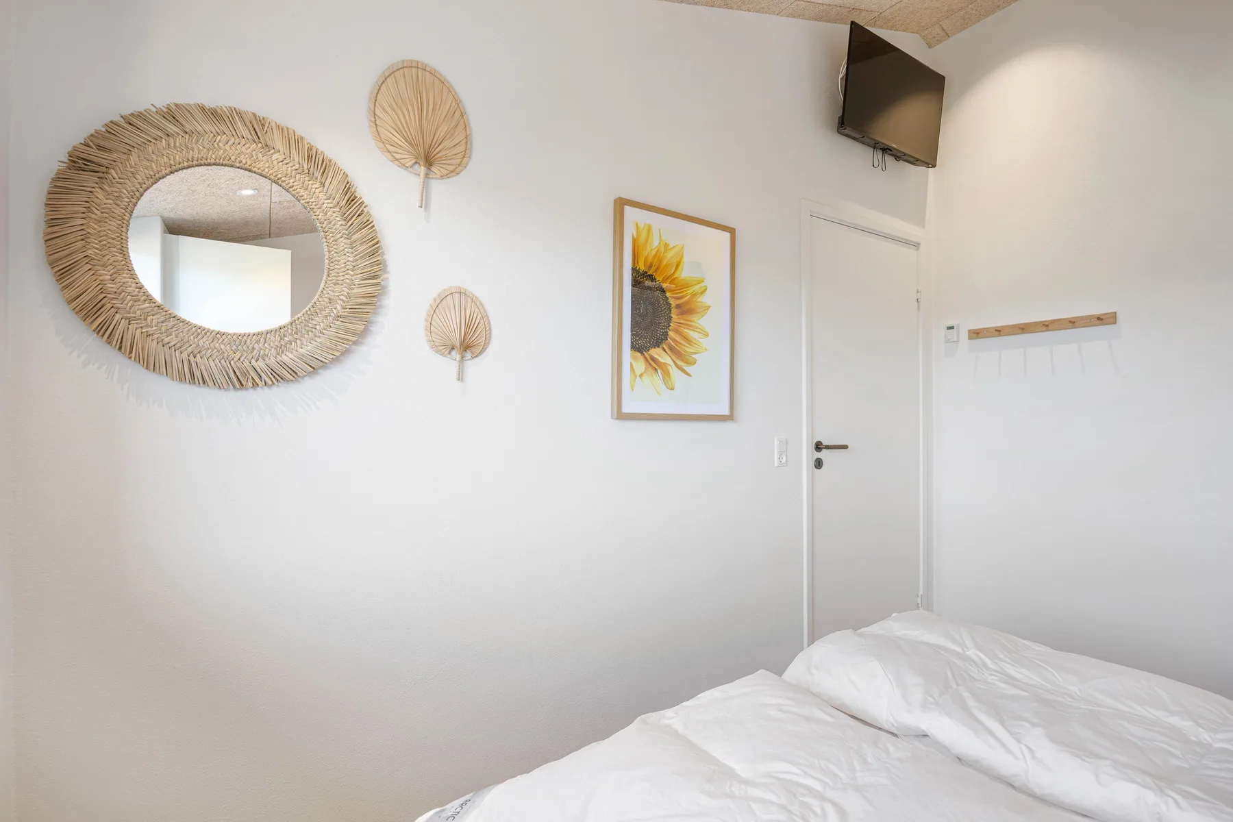Un dormitorio luminoso con ropa de cama blanca, arte en la pared y un televisor.