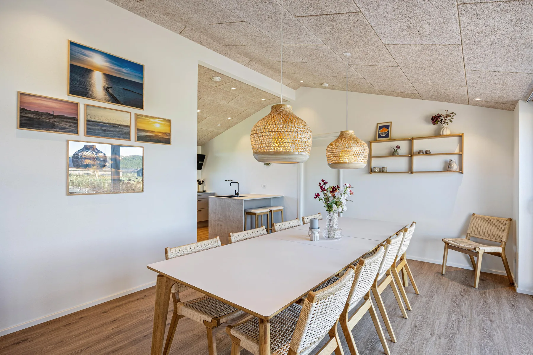 Comedor con una mesa larga y asientos tejidos junto a la cocina.