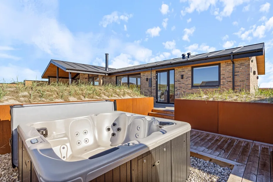 Una bañera de hidromasaje exterior está en una terraza frente a una casa moderna.