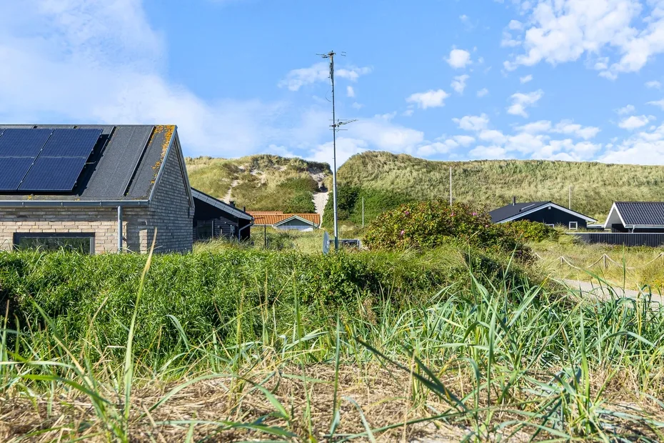 Un paisaje costero cubierto de hierba, con casas y paneles solares bajo un cielo azul.