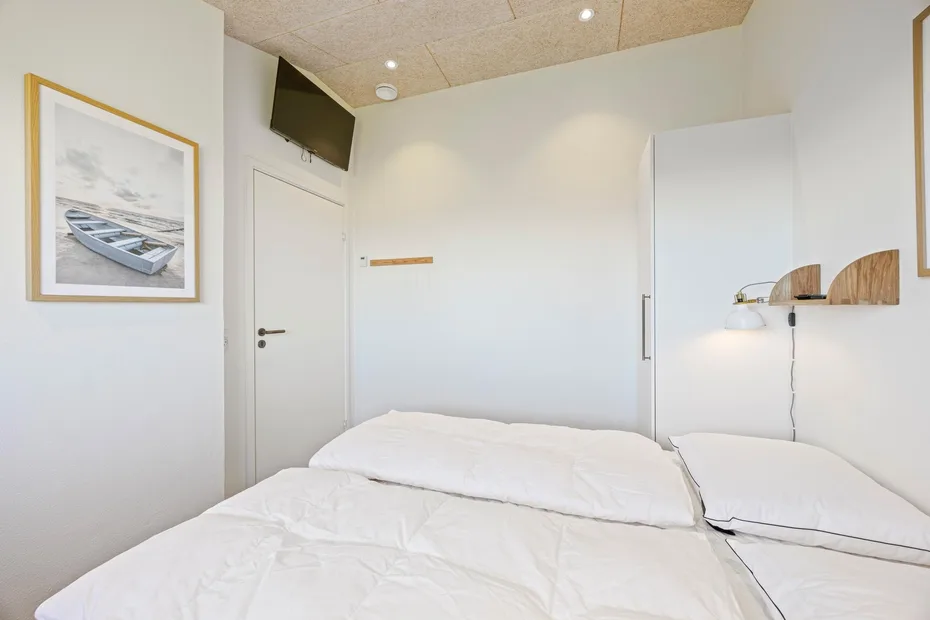 Un dormitorio luminoso con ropa de cama blanca y una lámina enmarcada en la pared.