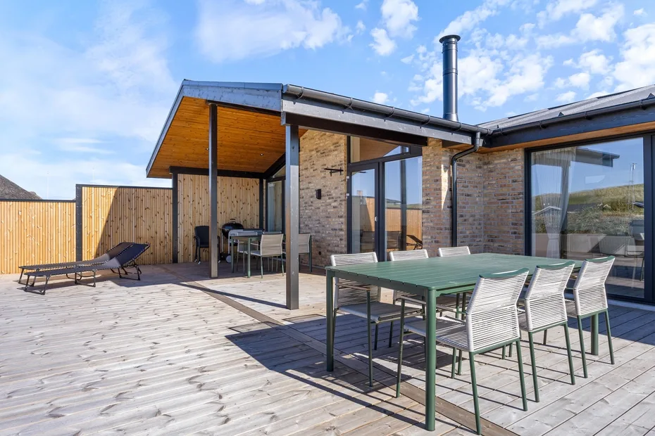 Una casa moderna da a una amplia terraza de madera con muebles de comedor al aire libre.