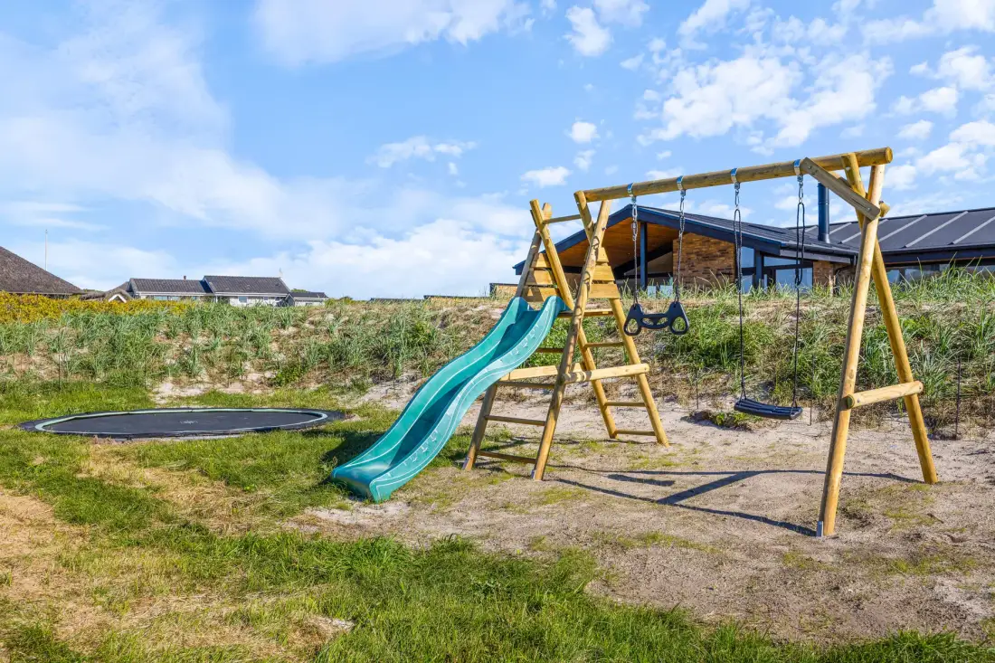 Zona de juegos al aire libre con estructura de madera, tobogán y columpios.