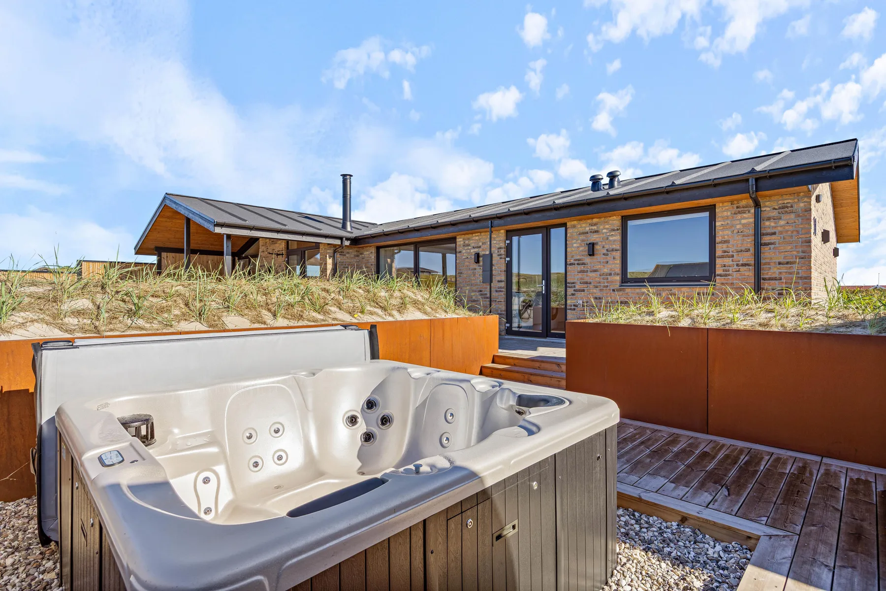 Una bañera de hidromasaje está en una terraza de madera junto a una casa moderna.