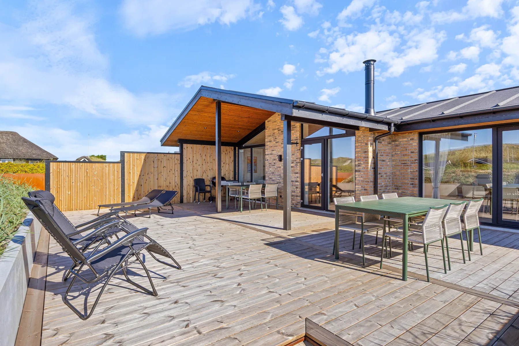 Una terraza de madera con asientos y tumbonas junto a una casa moderna.