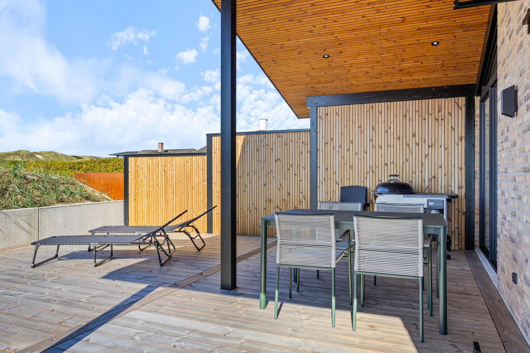 Comedor exterior cubierto con mesa y asientos sobre una terraza de madera.