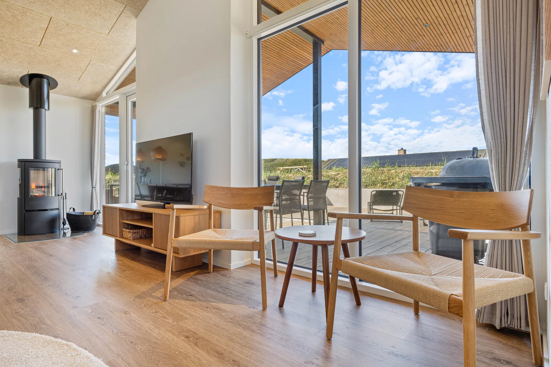 Una luminosa sala de estar con asientos y grandes ventanales con vistas a una terraza exterior.