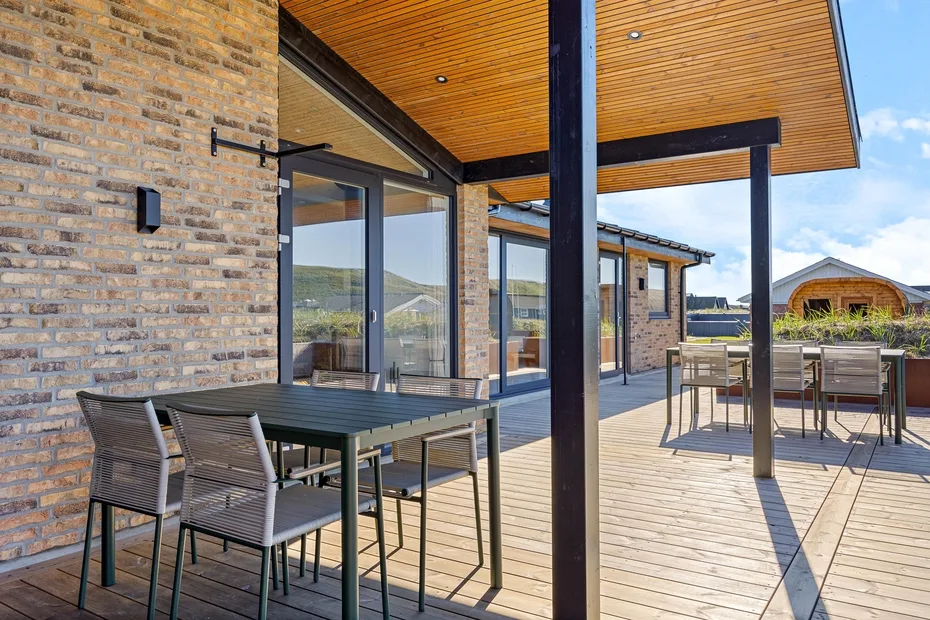 Comedor exterior cubierto con mesas y asientos junto a grandes puertas de vidrio.