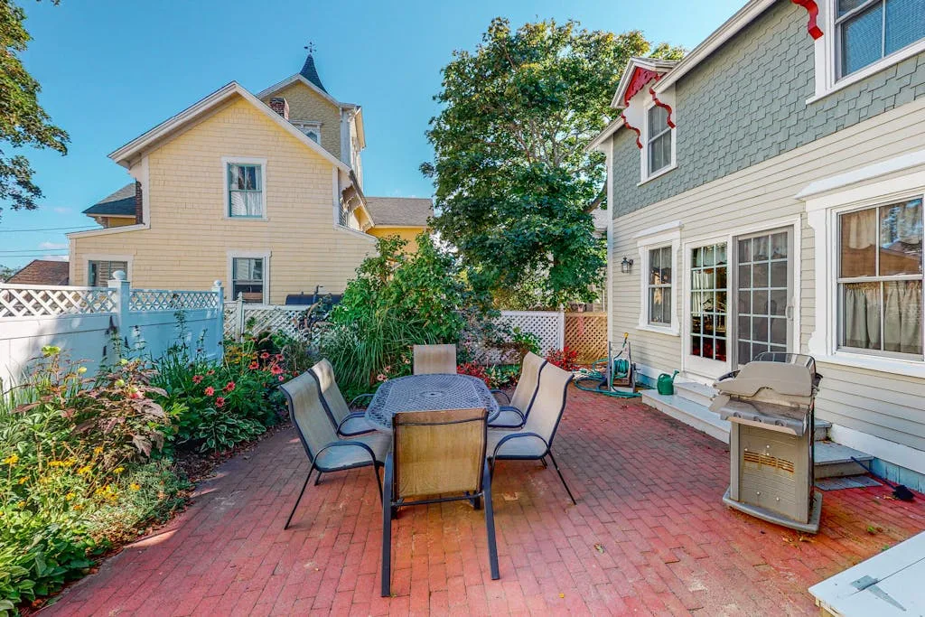 An outdoor patio with seating, a table, and a small grill beside the house.
