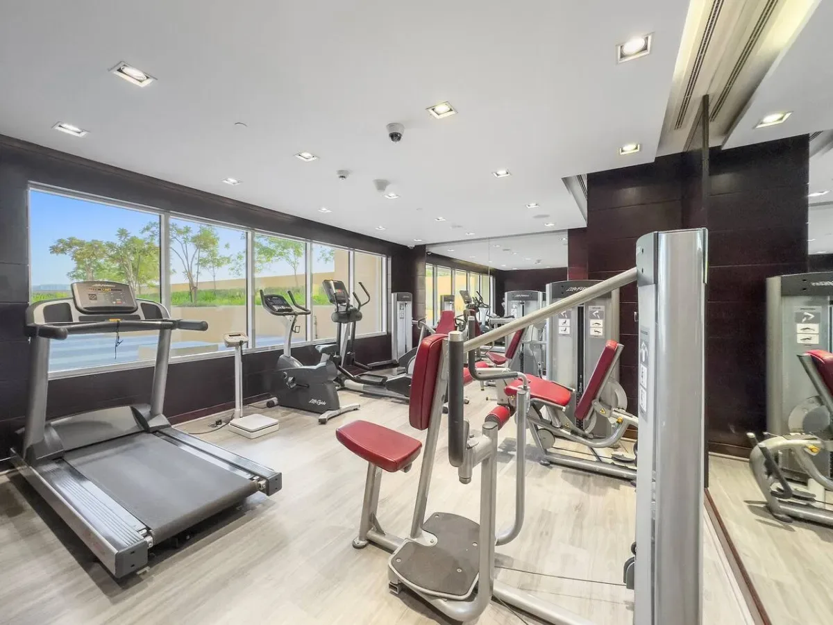 A gym with exercise machines and large windows overlooking a landscaped area.