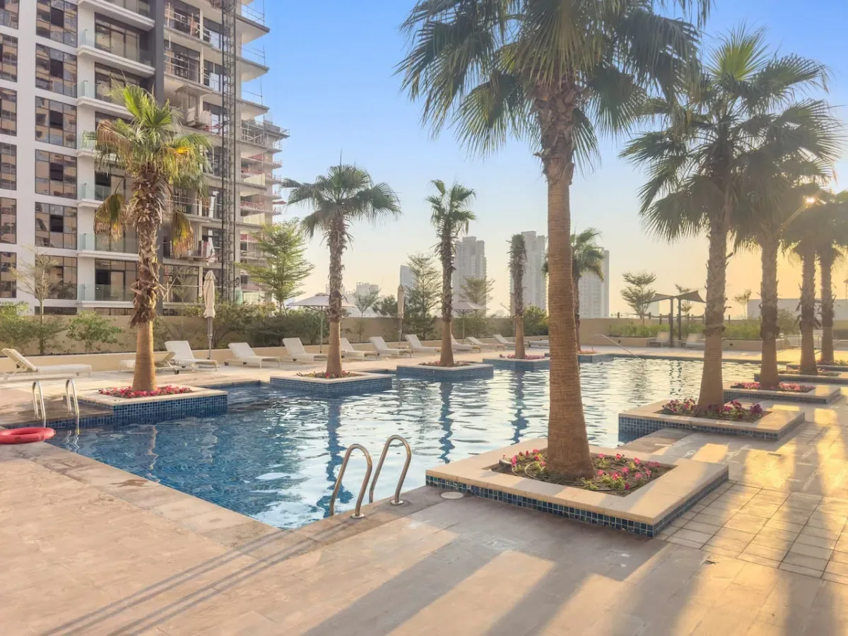 An outdoor swimming pool is surrounded by palm trees and lounge seating.