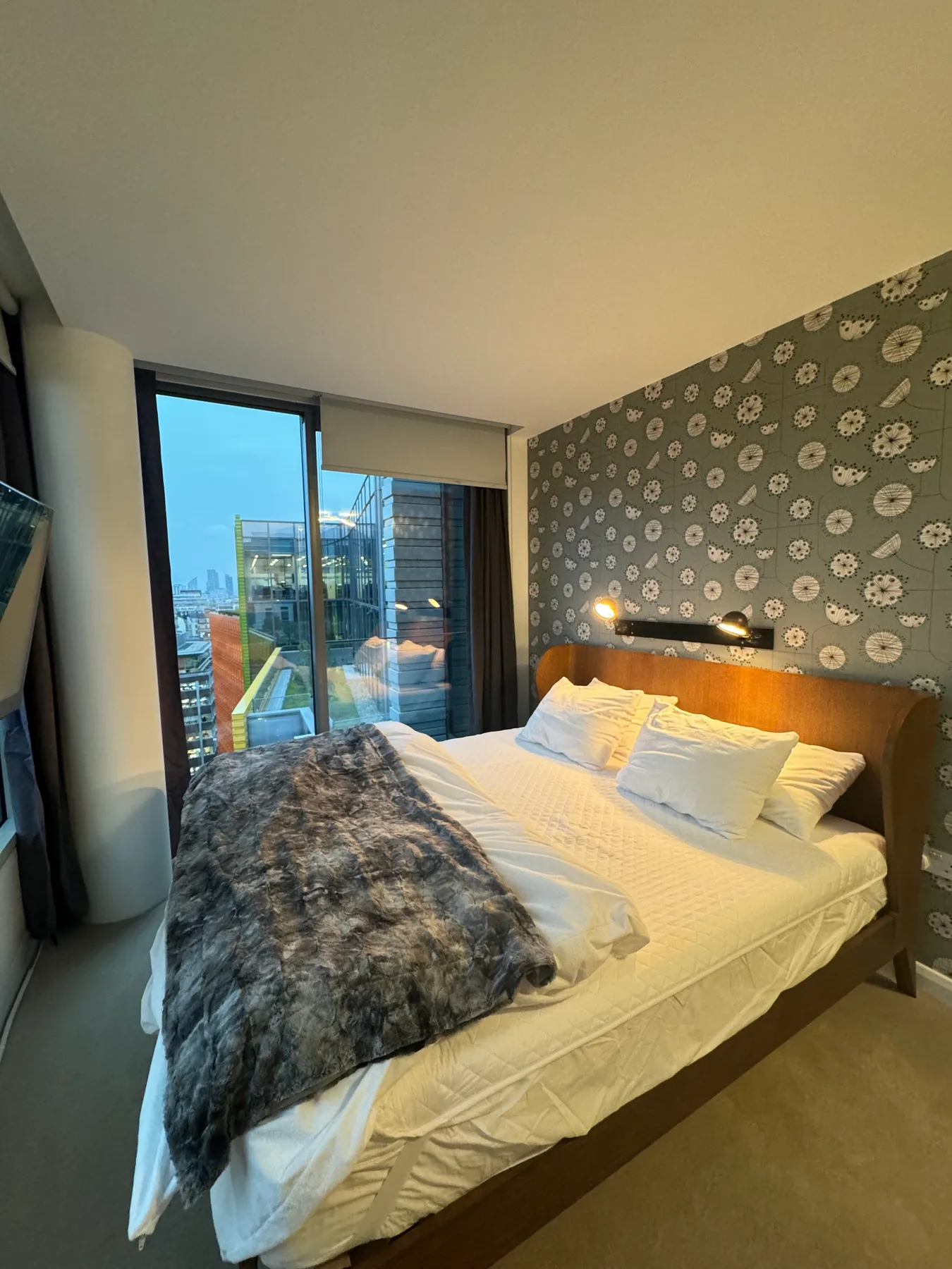 A bedroom with a bed beside a large glass window.