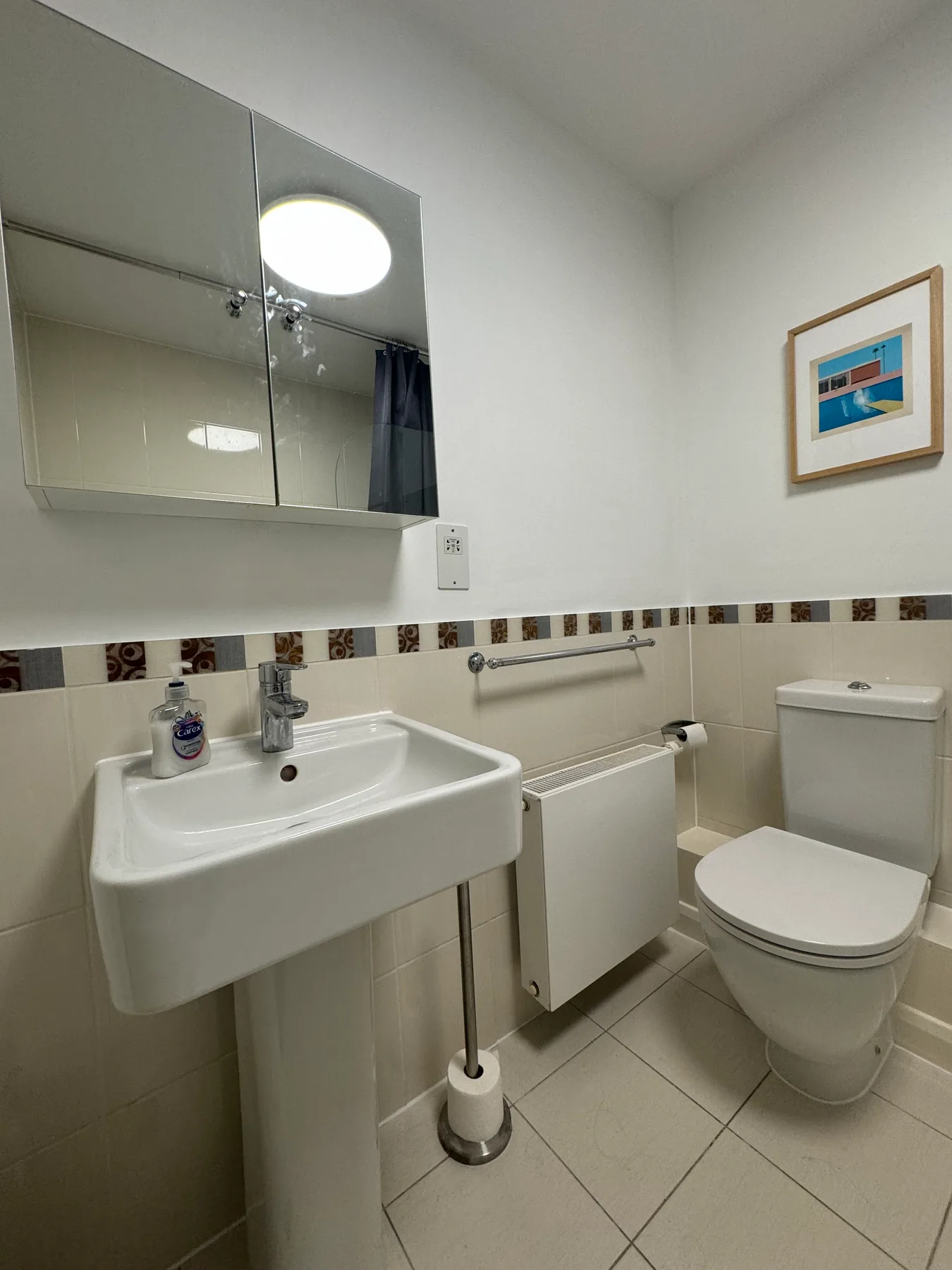 A compact bathroom with a sink, toilet, and framed artwork.