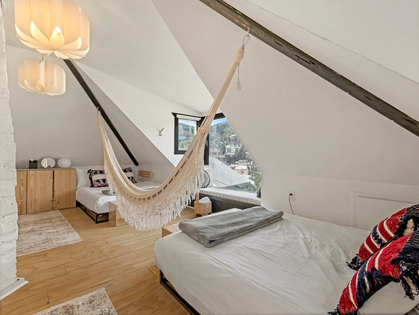 Un dormitorio abuhardillado luminoso con una hamaca colgada sobre la cama.