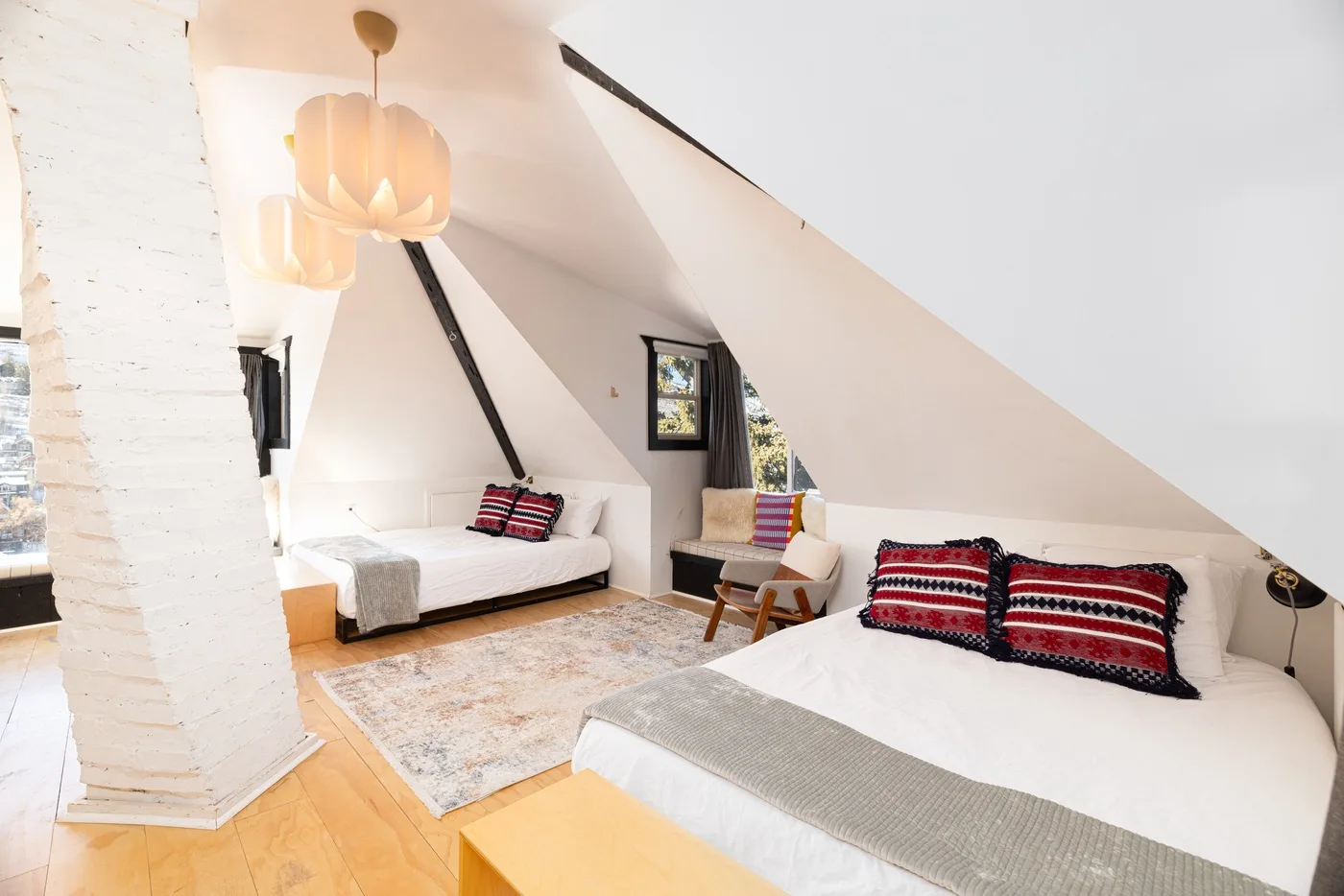 Un dormitorio abuhardillado y luminoso tiene camas bajo techos inclinados y una alfombra estampada.
