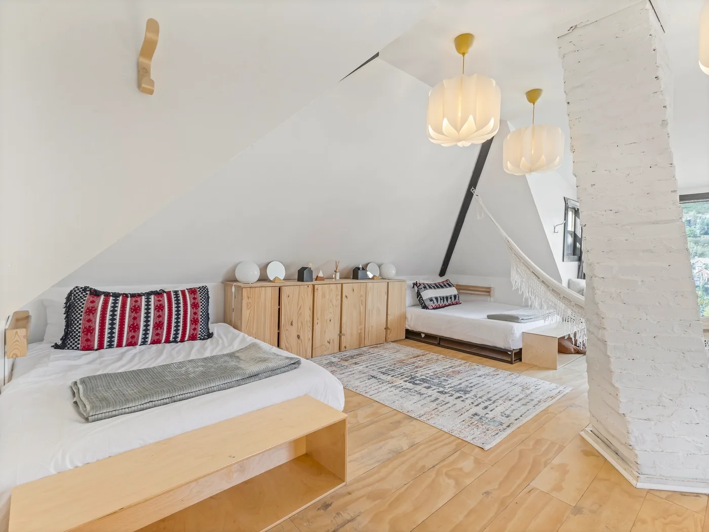Un dormitorio luminoso con dos camas bajas y un mueble de madera bajo un techo inclinado.