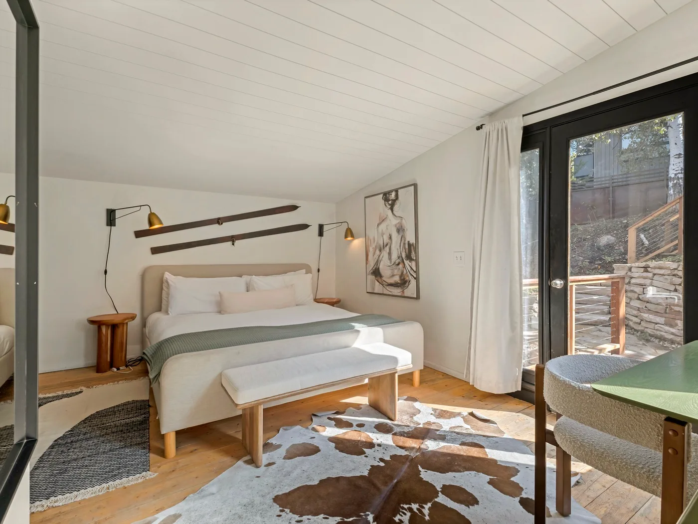 Un dormitorio luminoso con una cama, un banco y puertas de vidrio que dan a un patio.