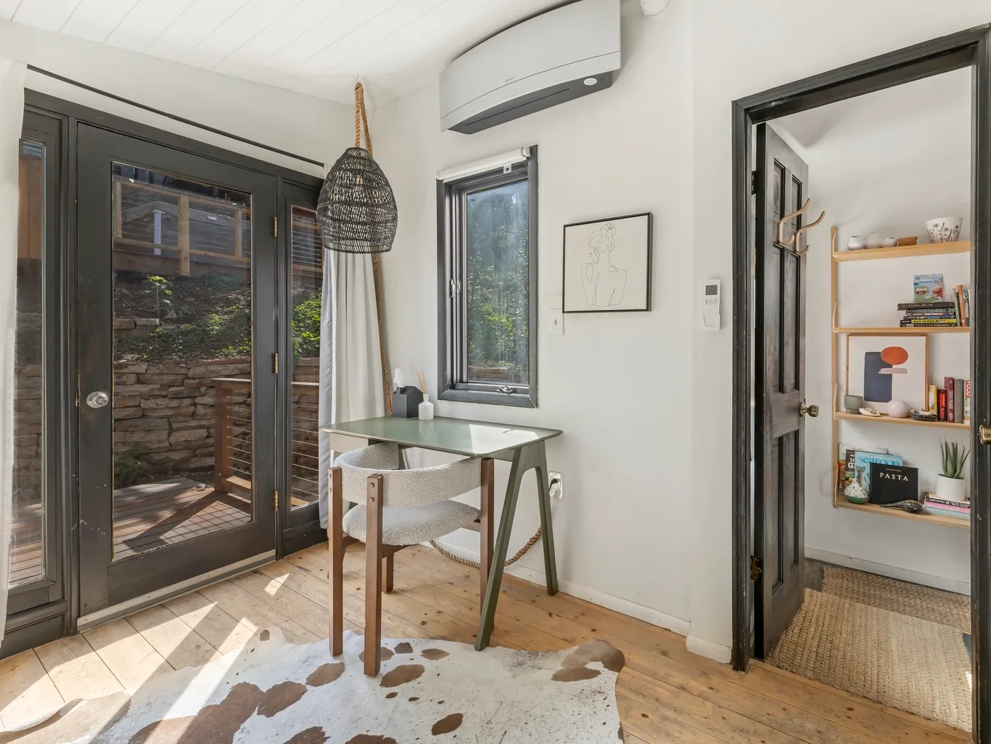 Una habitación luminosa con una mesa pequeña junto a una puerta de vidrio y una ventana.