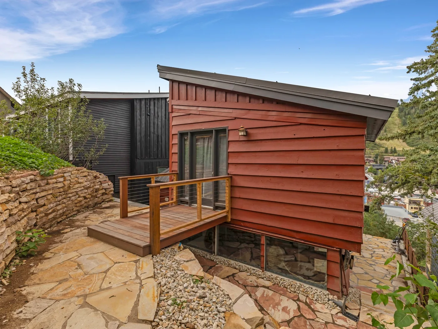 Un edificio de revestimiento rojo junto a una zona exterior pavimentada con piedra y una terraza de madera.