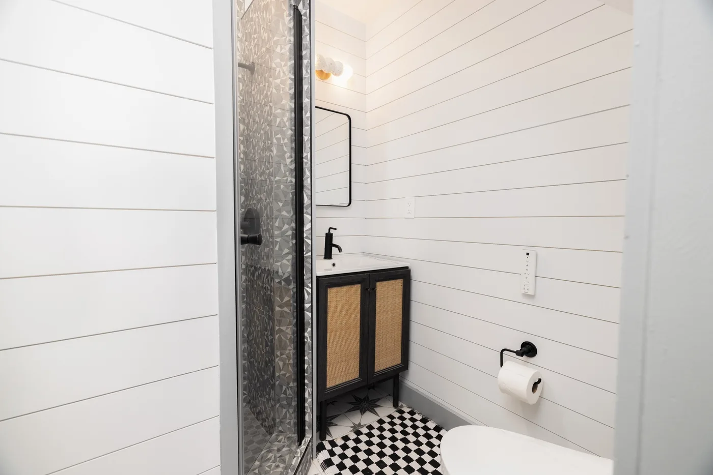 Un baño compacto con ducha de vidrio, lavabo y suelo de baldosas blancas y negras.