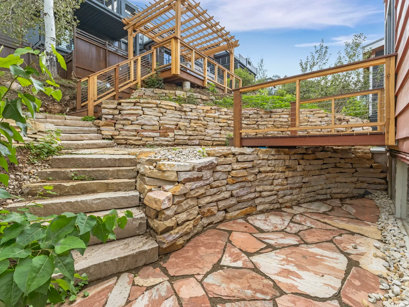 Un patio exterior con pavimento de piedra, escalones y una terraza con barandilla de madera.